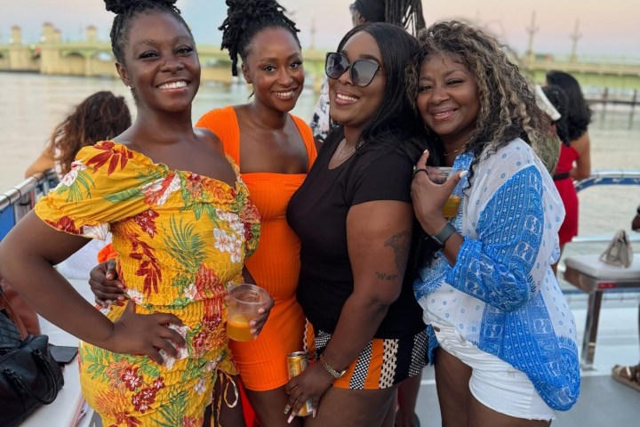 Four women smiling on a boat deck at sunset.
