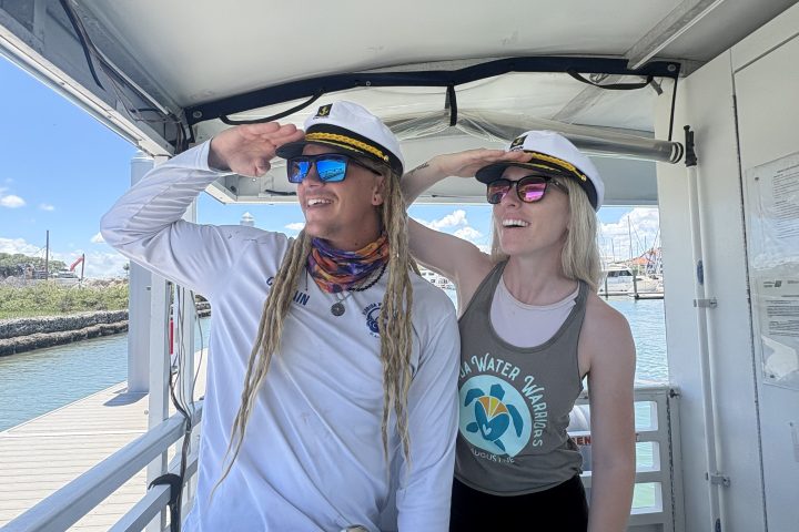 Two people wearing captain hats smiling on a boat's deck.