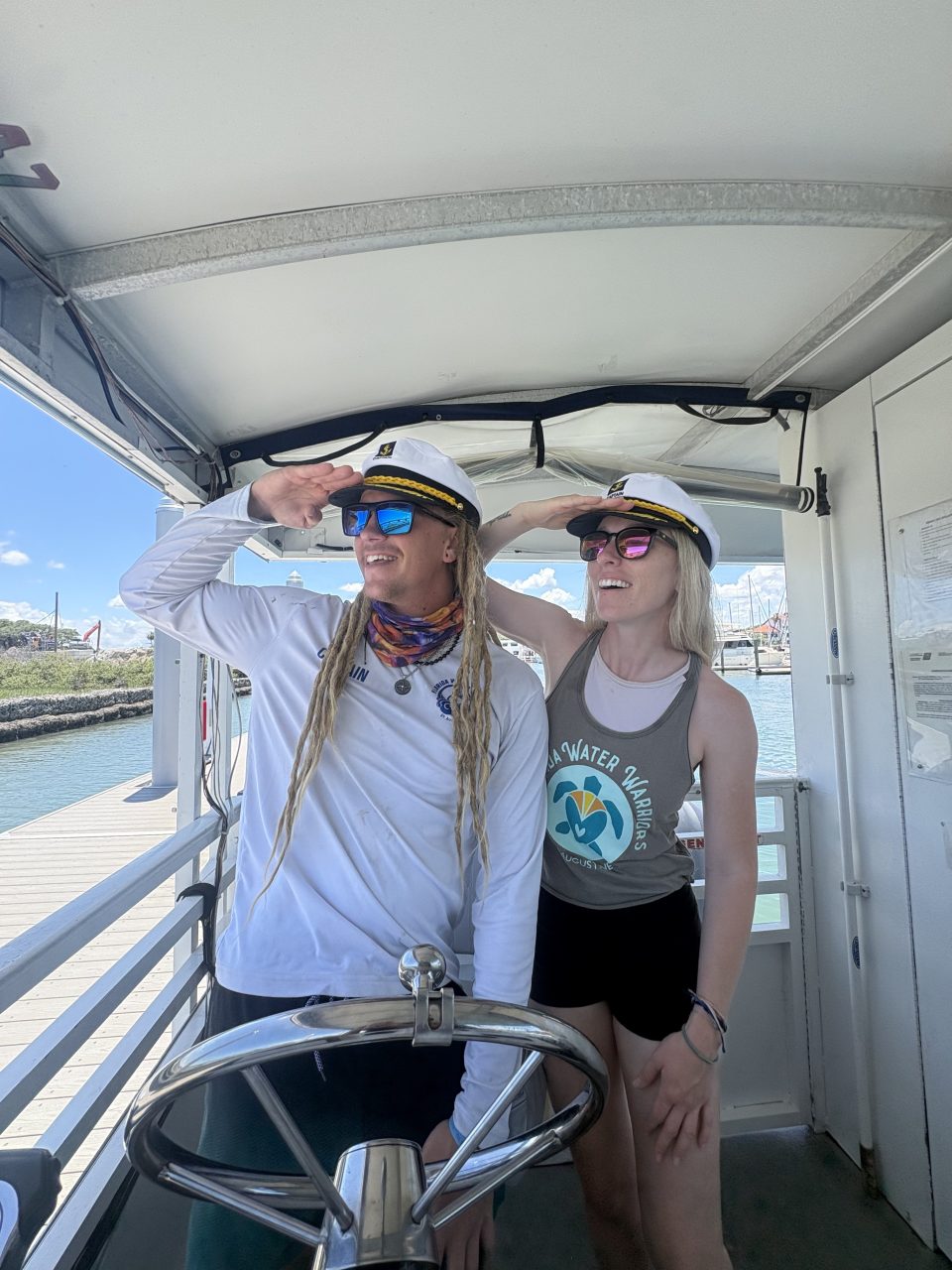 Two people wearing captain hats smiling on a boat's deck.