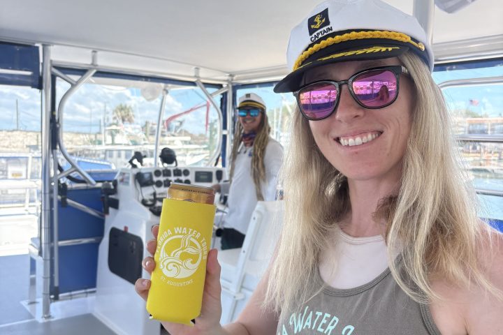 Woman in captain's hat holds a yellow cup on a boat.