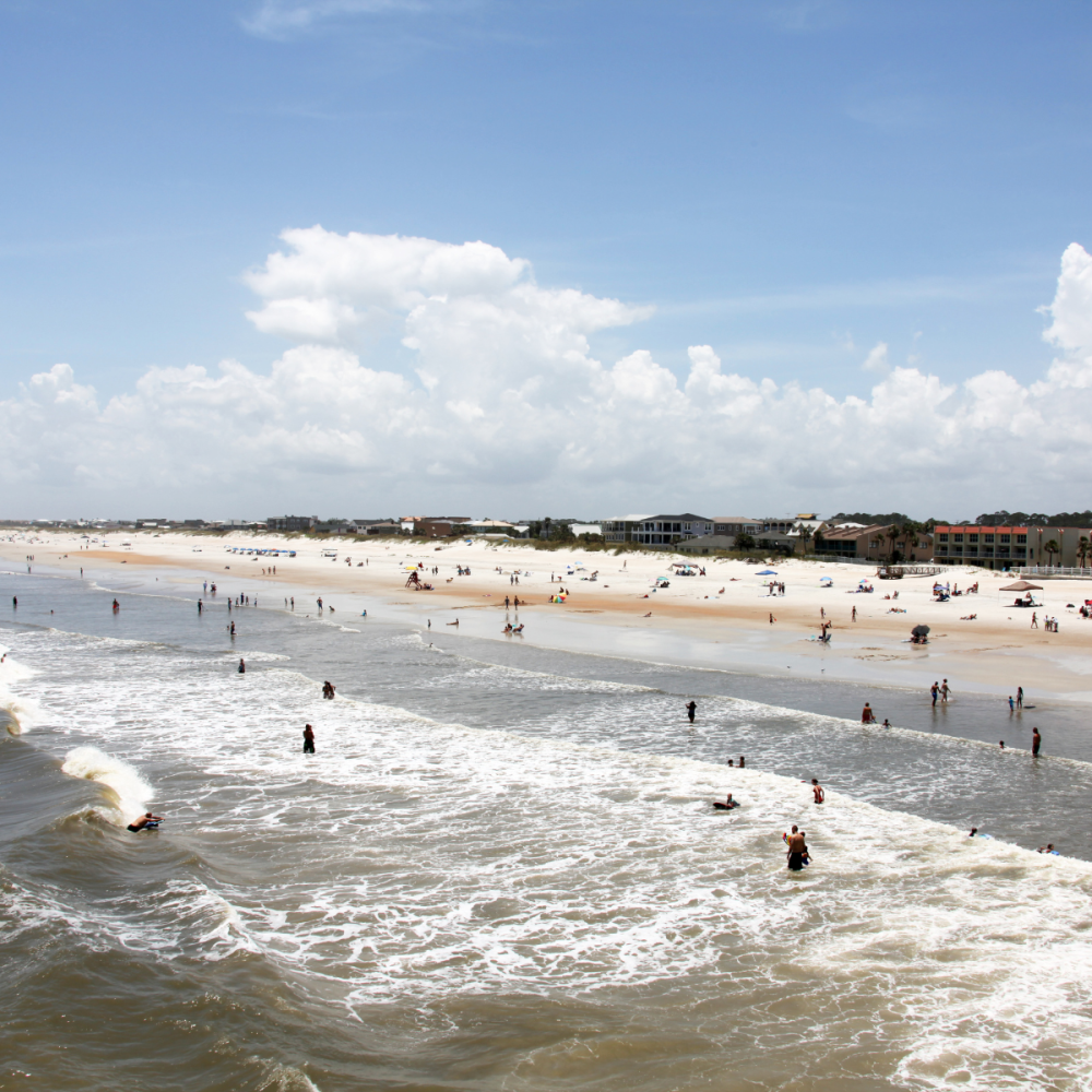 People enjoying a sunny day at the beach with waves and distant buildings.