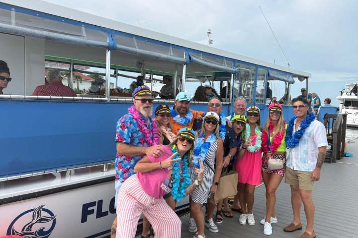 Group in colorful leis and captain hats posing on a dock by a blue boat.