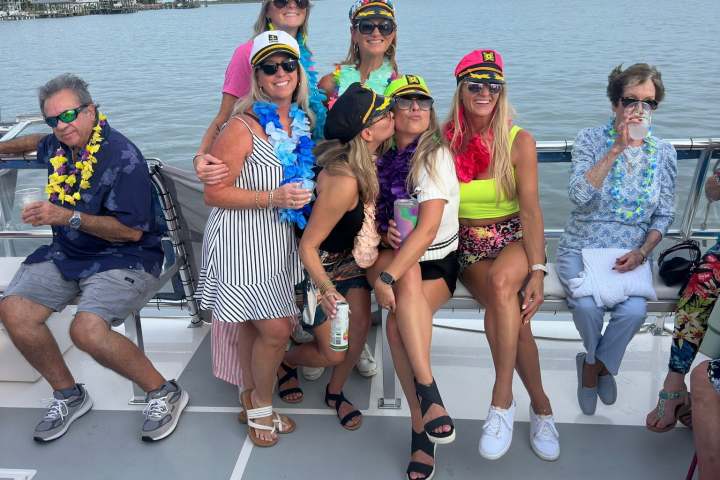 Group of people wearing hats and leis sitting on a boat deck.