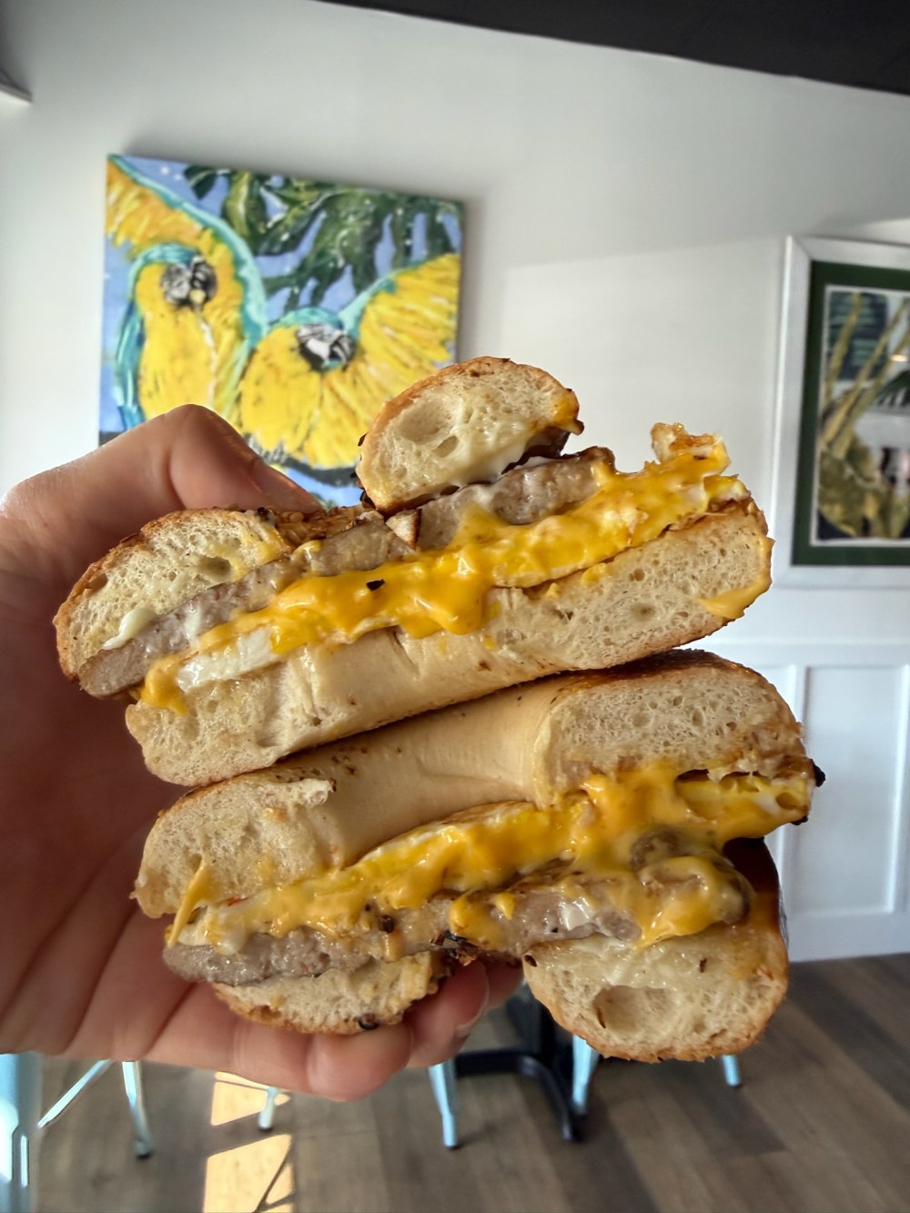 Hand holding sliced bagel with cheese and meat filling.