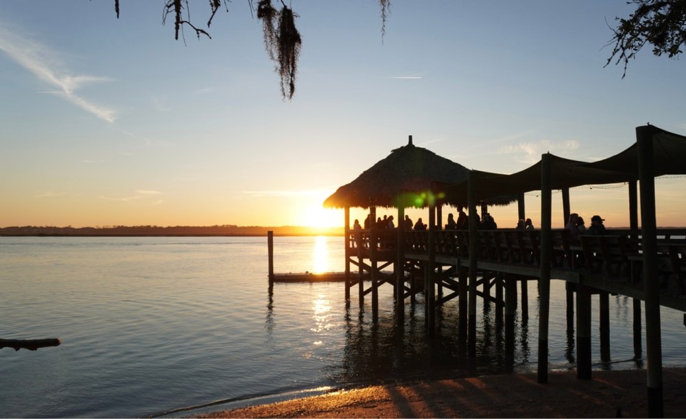 Silhouetted pier with people at sunset over calm water.