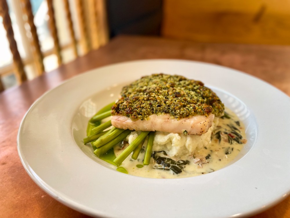 Salmon with herb crust on asparagus and creamy sauce on a white plate.