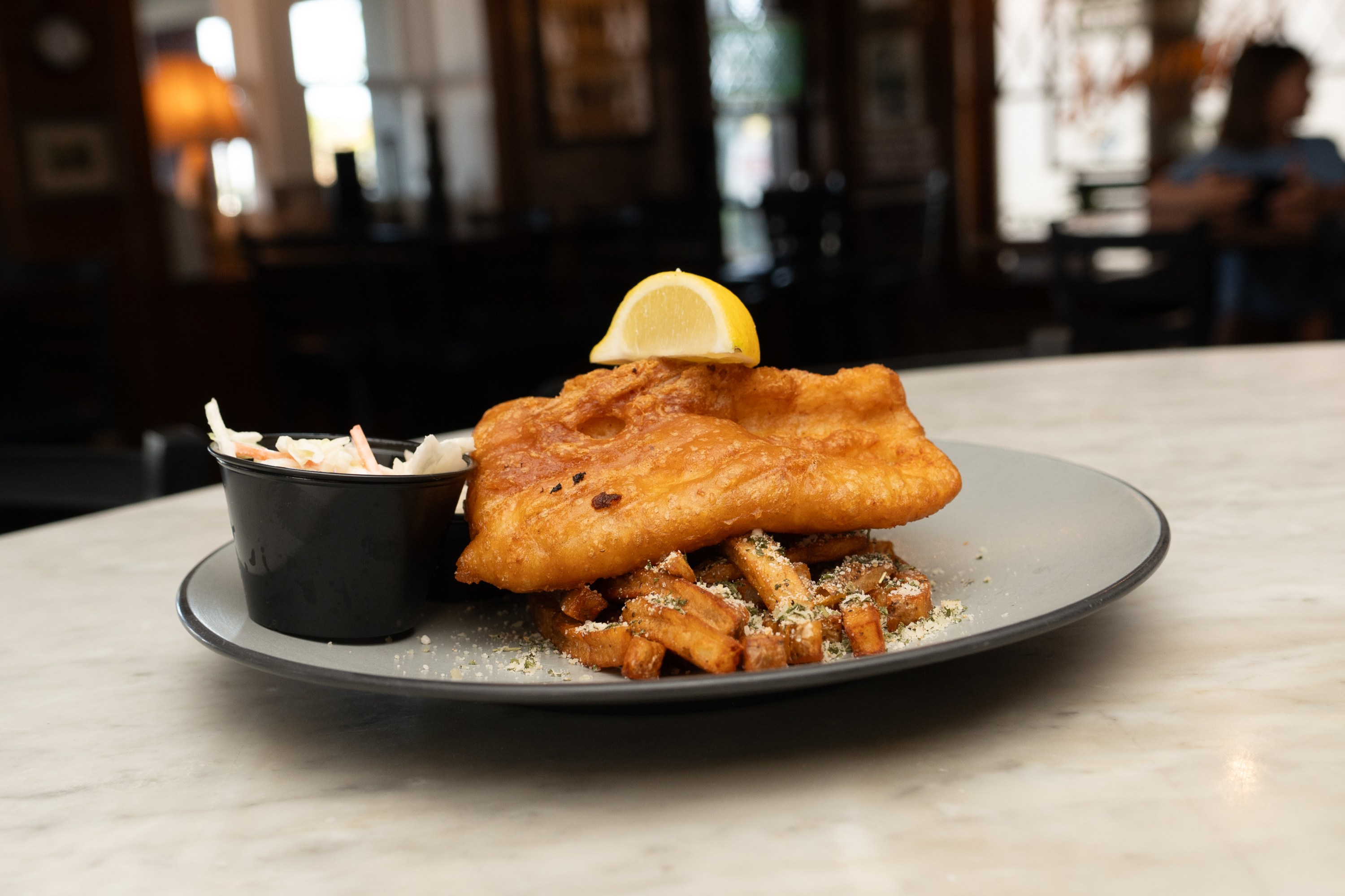 Plate of fish and chips with coleslaw on a marble table.