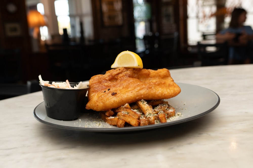 Plate of fish and chips with coleslaw on a marble table.