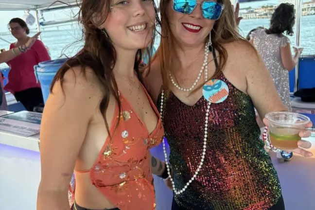 Two women smiling, holding drinks on a boat with festive attire and decorations.