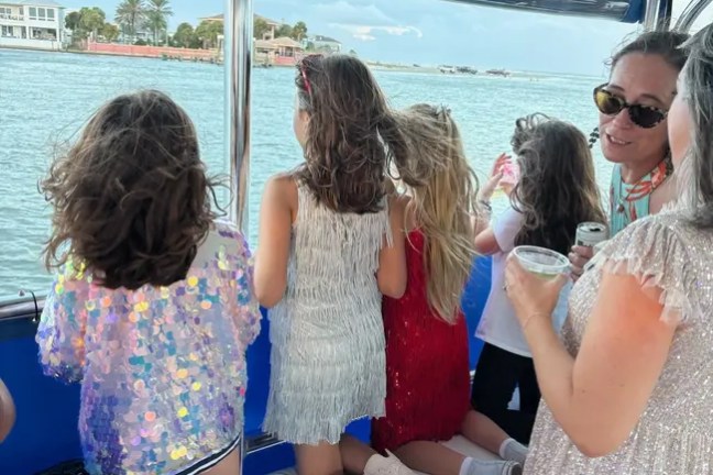 Children in sparkly dresses on a boat, looking over water with an adult.