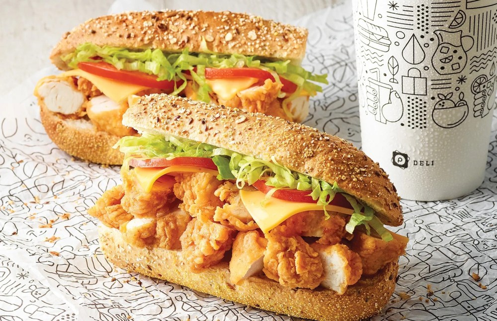 Two chicken sandwiches with lettuce and tomato on seeded buns next to a decorated cup.