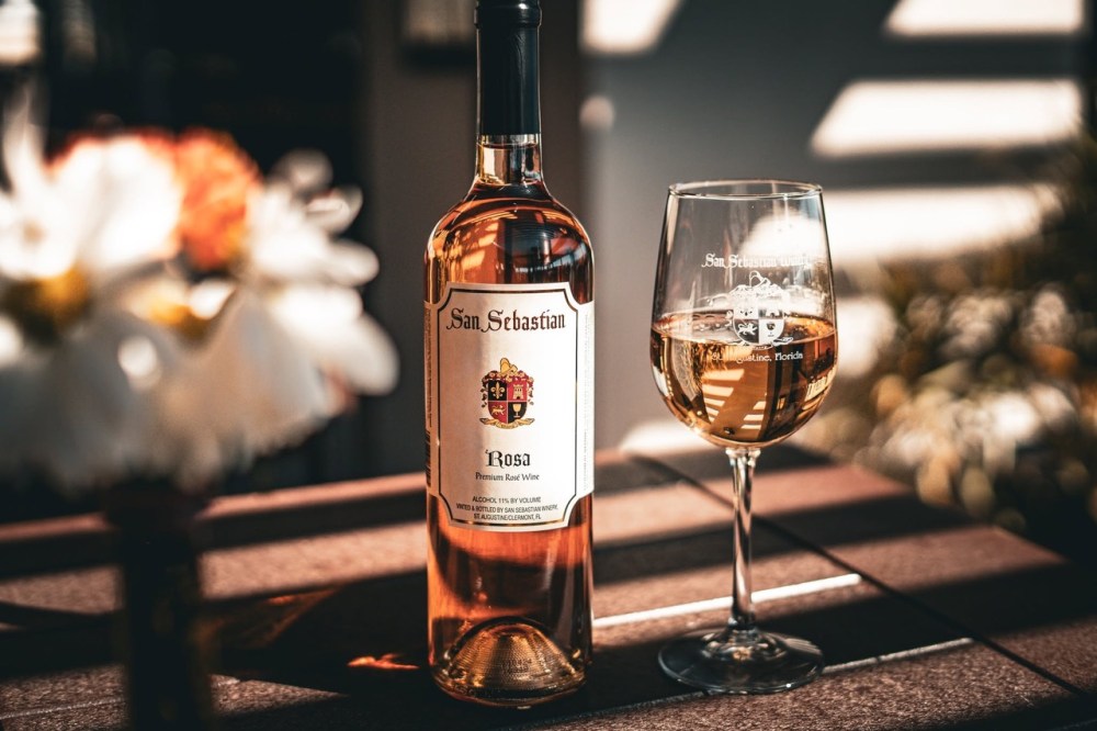 Bottle and glass of rosé wine on a table in sunlight.