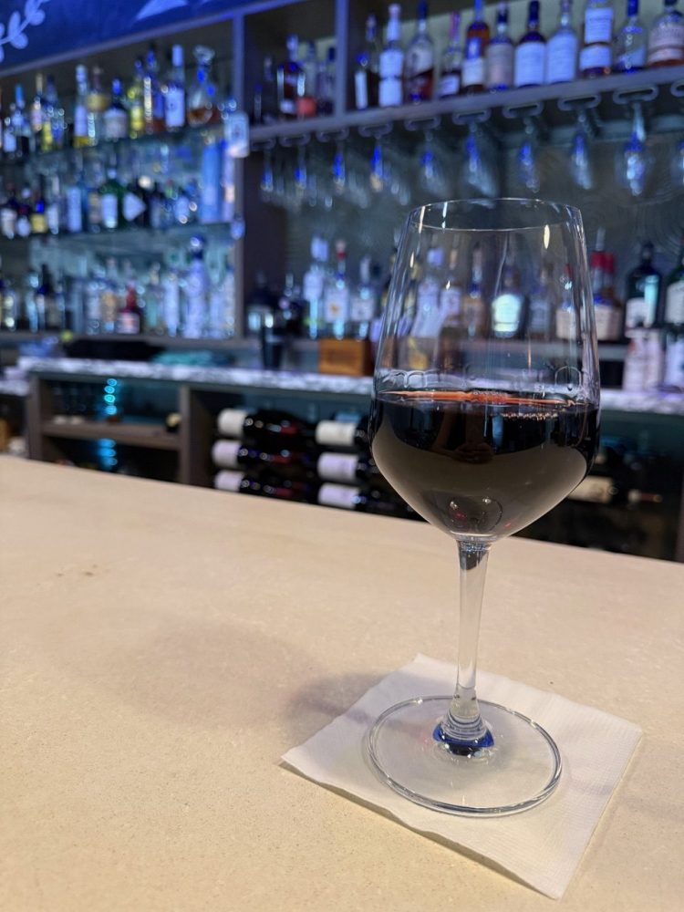 Glass of red wine on a bar counter with bottles in the background.