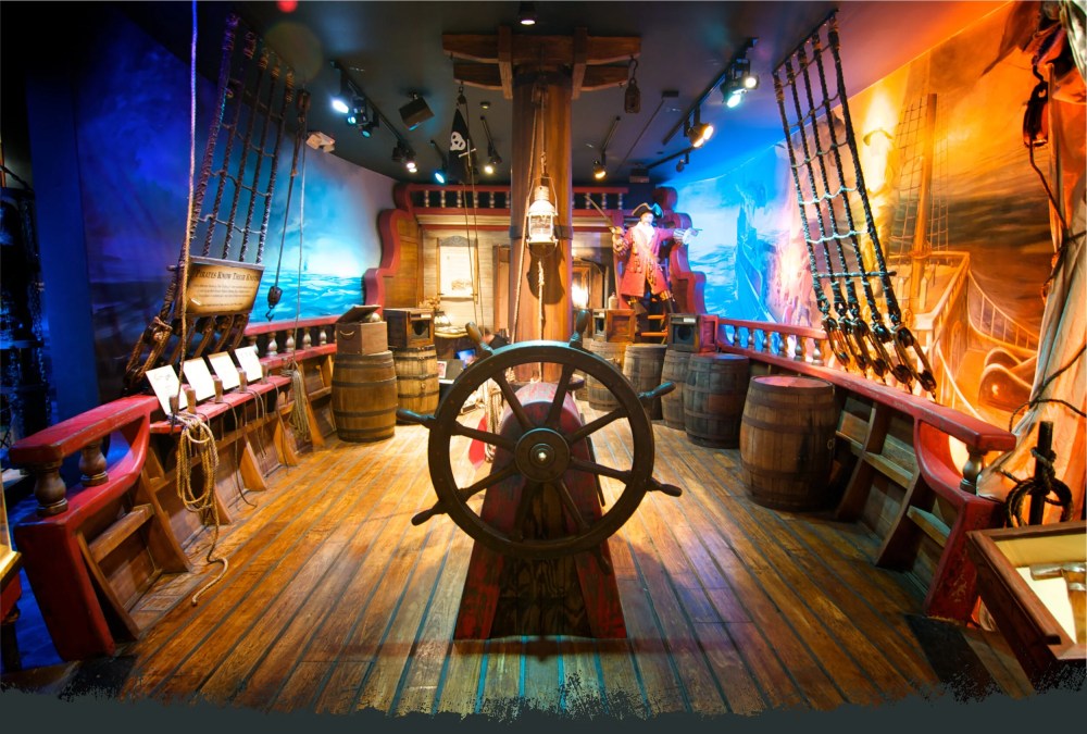 Colorful pirate ship interior exhibit with a large steering wheel and decorative elements.